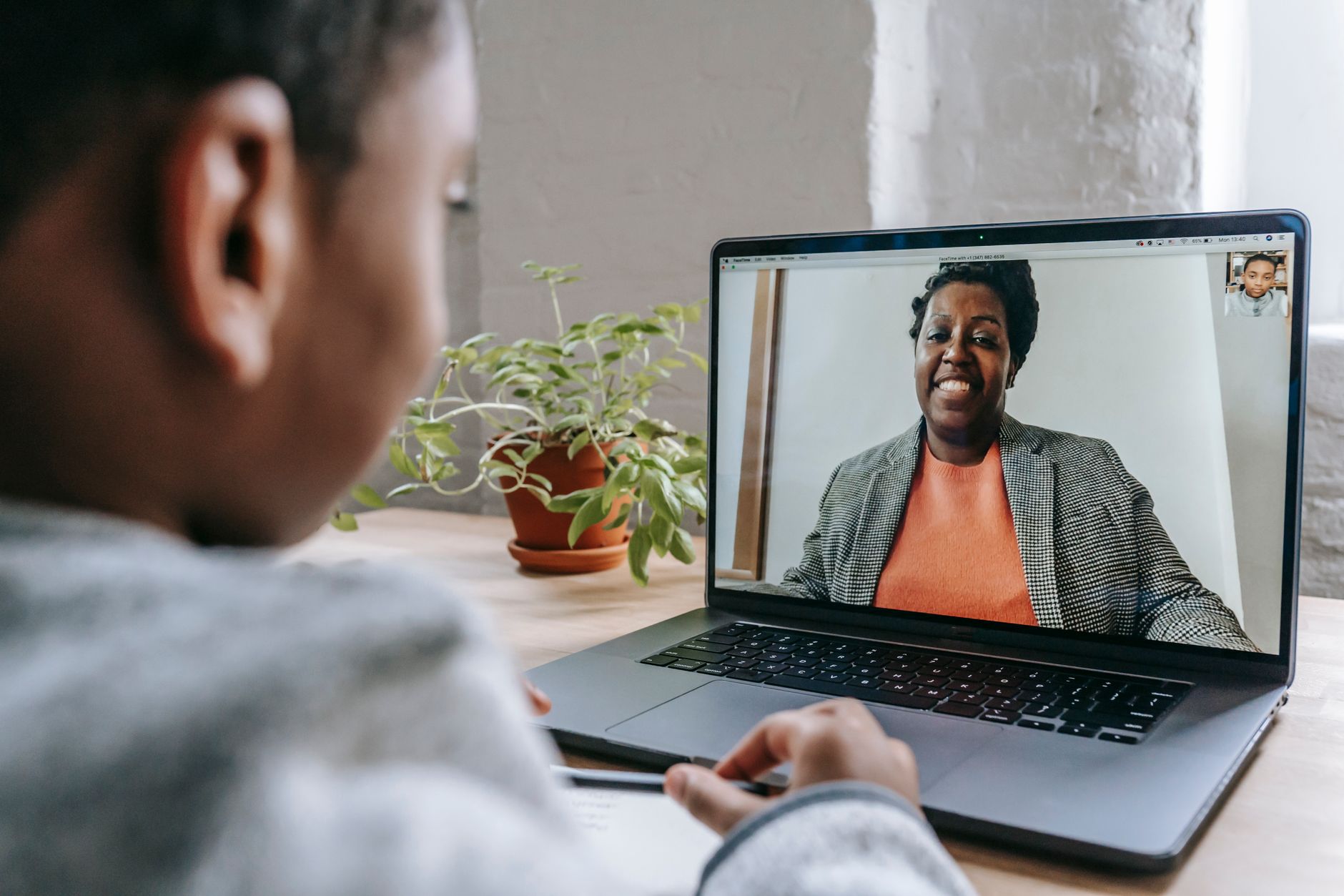 A learner at a desk watching a smiling tutor on a laptop screen during a one-to-one video lesson